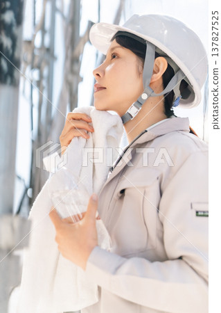 夏季建築工地採取的預防中暑措施。一名女工在工作間隙用毛巾擦汗並補充水分。 137827525