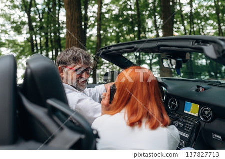 Road near the trees. Senior couple driving convertible cabriolet car Road near the trees. Senior couple driving convertible cabriolet car 137827713