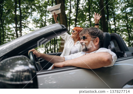 Hands are up, happy woman is with hat. Senior couple driving convertible cabriolet car Hands are up, happy woman is with hat. Senior couple driving convertible cabriolet car 137827714