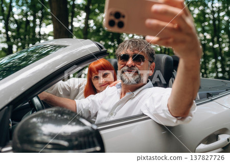 Time for a selfie. Senior couple driving convertible cabriolet car Time for a selfie. Senior couple driving convertible cabriolet car 137827726