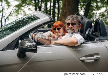 Wearing sunglasses, side view. Senior couple driving convertible cabriolet car Wearing sunglasses, side view. Senior couple driving convertible cabriolet car 137827733