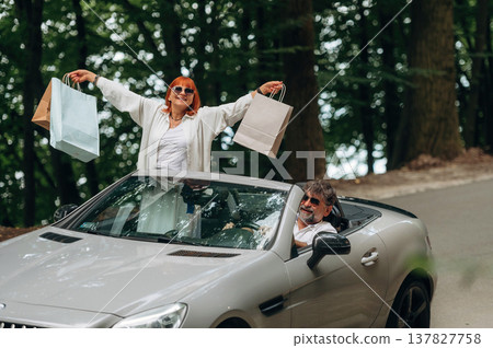Paper shopping bags in hands of woman. Senior couple driving convertible cabriolet car 137827758
