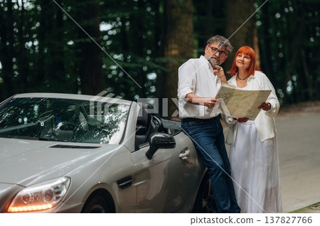 Reading the map. Lovely senior couple standing on the road near convertible cabriolet car Reading the map. Lovely senior couple standing on the road near convertible cabriolet car 137827766