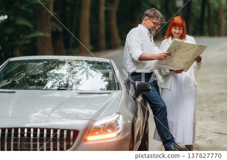 Reading the map. Lovely senior couple standing on the road near convertible cabriolet car Reading the map. Lovely senior couple standing on the road near convertible cabriolet car 137827770