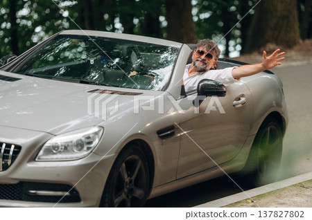 Looking at the camera. Stylish senior man is in convertible cabriolet car Looking at the camera. Stylish senior man is in convertible cabriolet car 137827802