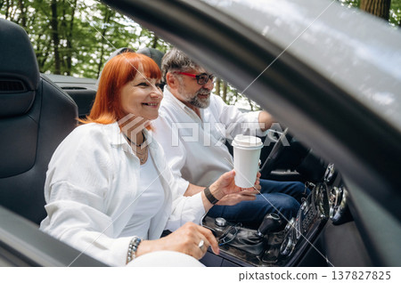 Cup of drink in woman's hand. Senior couple driving convertible cabriolet car 137827825