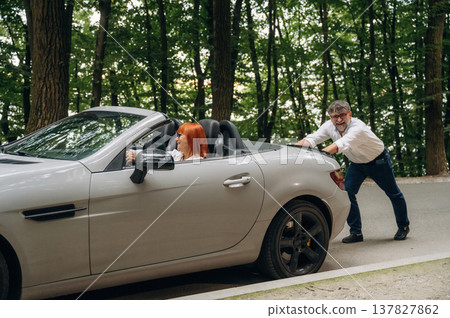 Man pushing a stalled convertible car, woman driving 137827862