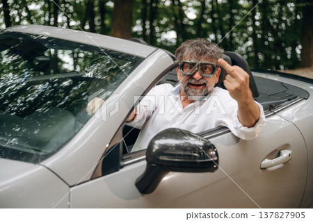 Middle finger up, don't care, cool attitude. Stylish senior man is in convertible cabriolet car Middle finger up, don't care, cool attitude. Stylish senior man is in convertible cabriolet car 137827905