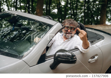 Middle finger up, don't care, cool attitude. Stylish senior man is in convertible cabriolet car Middle finger up, don't care, cool attitude. Stylish senior man is in convertible cabriolet car 137827906