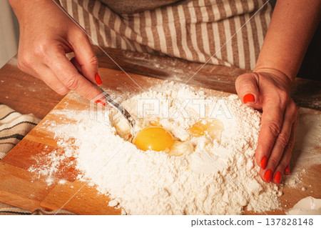 Hands mixing eggs into flour on wooden surface for baking at home kitchen during bright day 137828148