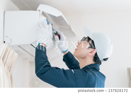 Internal inspection of an air conditioner. A male engineer in work clothes performs repair work using a screwdriver. 137828172