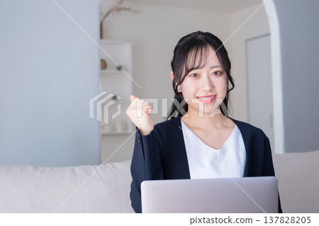 A woman in her 20s makes a triumphant gesture while working on her computer. 137828205