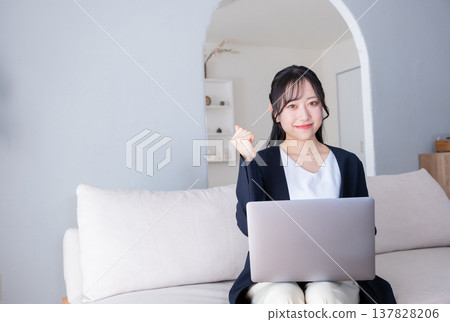A woman in her 20s makes a triumphant gesture while working on her computer. A woman in her 20s makes a triumphant gesture while working on her computer. 137828206
