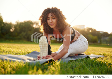 Stretching the legs. Young fitness woman is on the field outdoors Stretching the legs. Young fitness woman is on the field outdoors 137828209
