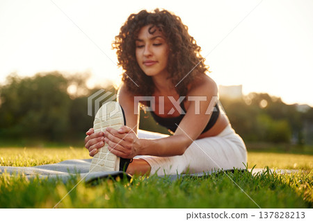 Flexibility exercise for legs. Young fitness woman is on the field outdoors Flexibility exercise for legs. Young fitness woman is on the field outdoors 137828213