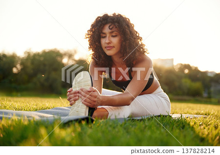 Flexibility exercise for legs. Young fitness woman is on the field outdoors 137828214