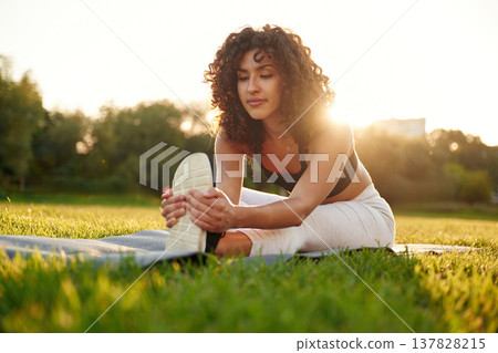 Flexibility exercise for legs. Young fitness woman is on the field outdoors 137828215