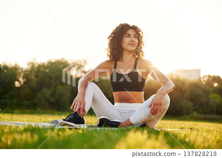 Sitting on the yoga mat. Young fitness woman is on the field outdoors Sitting on the yoga mat. Young fitness woman is on the field outdoors 137828218