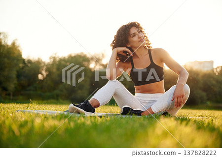 Sitting on the yoga mat. Young fitness woman is on the field outdoors Sitting on the yoga mat. Young fitness woman is on the field outdoors 137828222