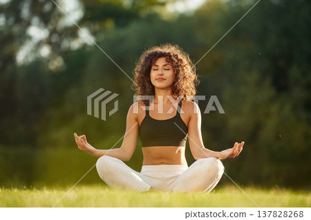 Meditation practice, in lotus pose. Young fitness woman is on the field outdoors Meditation practice, in lotus pose. Young fitness woman is on the field outdoors 137828268