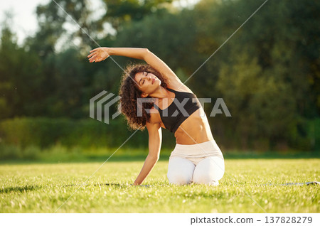 Raising hands up while sitting on the ground. Young fitness woman is on the field outdoors Raising hands up while sitting on the ground. Young fitness woman is on the field outdoors 137828279