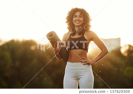 Evening dawn, against sunlight, standing and smiling. Young fitness woman is on the field outdoors Evening dawn, against sunlight, standing and smiling. Young fitness woman is on the field outdoors 137828309
