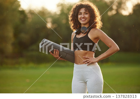 Evening dawn, against sunlight, standing and smiling. Young fitness woman is on the field outdoors Evening dawn, against sunlight, standing and smiling. Young fitness woman is on the field outdoors 137828313