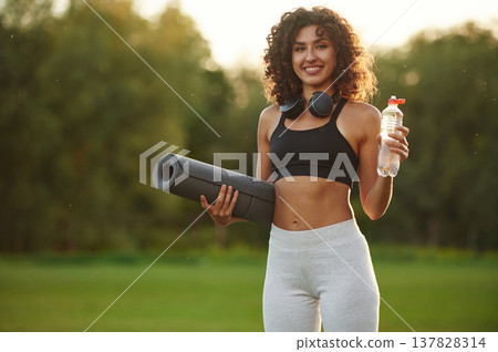 Hydration conception, holding bottle of water. Young fitness woman is on the field outdoors Hydration conception, holding bottle of water. Young fitness woman is on the field outdoors 137828314