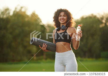 Hydration conception, holding bottle of water. Young fitness woman is on the field outdoors Hydration conception, holding bottle of water. Young fitness woman is on the field outdoors 137828315