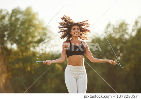 Jumping rope, active. Young fitness woman is on the field outdoors Jumping rope, active. Young fitness woman is on the field outdoors 137828357