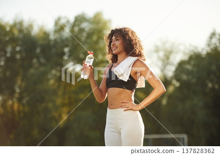 Drinking water from a bottle. Young fitness woman is on the field outdoors Drinking water from a bottle. Young fitness woman is on the field outdoors 137828362