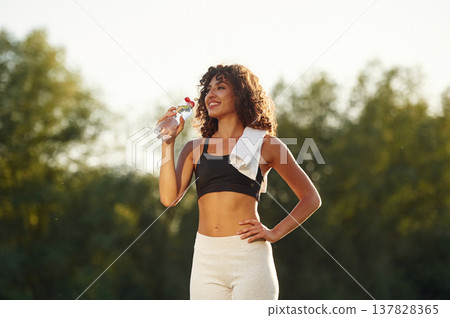 Drinking water from a bottle. Young fitness woman is on the field outdoors 137828365