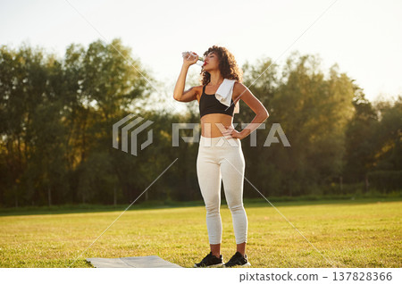 Drinking water from a bottle. Young fitness woman is on the field outdoors 137828366