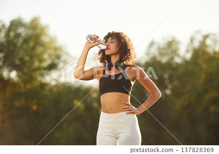 Break time, with bottle of water. Young fitness woman is on the field outdoors Break time, with bottle of water. Young fitness woman is on the field outdoors 137828369