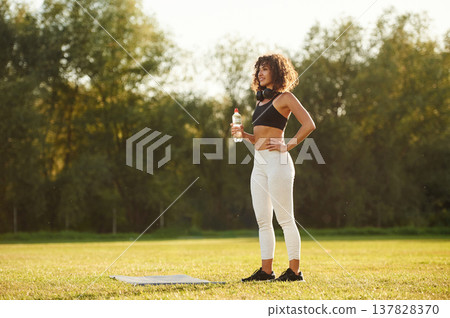 Break time, with bottle of water. Young fitness woman is on the field outdoors Break time, with bottle of water. Young fitness woman is on the field outdoors 137828370