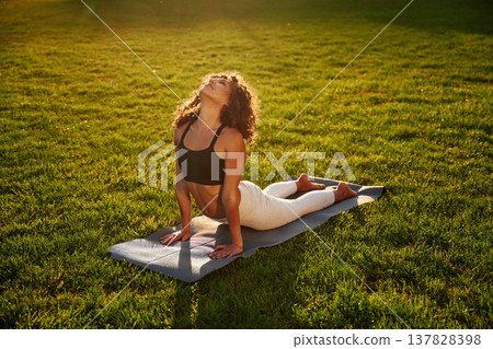On the fitness mat, doing exercises. Young fitness woman is on the field outdoors On the fitness mat, doing exercises. Young fitness woman is on the field outdoors 137828398