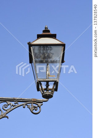Vintage gas lamp on ornate metal bracket against blue sky Vintage gas lamp on ornate metal bracket against blue sky 137828540