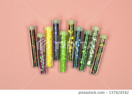 A stunning flat lay of multi-colored sequins in tiny transparent containers, glowing against a pink surface A stunning flat lay of multi-colored sequins in tiny transparent containers, glowing against a pink surface 137828582