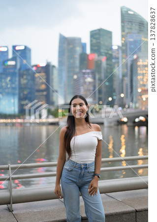 Asian tourist woman posing by the waterfront at Marina Bay Singapore during evening Asian tourist woman posing by the waterfront at Marina Bay Singapore during evening 137828637