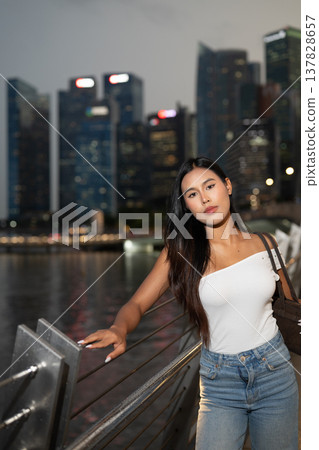 Asian tourist woman posing by the waterfront at Marina Bay Singapore during evening Asian tourist woman posing by the waterfront at Marina Bay Singapore during evening 137828657