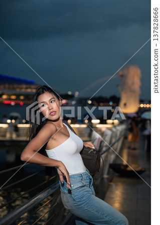 Asian tourist woman posing by the waterfront at Marina Bay Singapore during evening Asian tourist woman posing by the waterfront at Marina Bay Singapore during evening 137828666