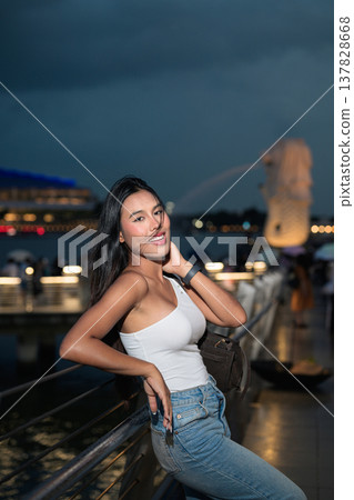 Asian tourist woman posing by the waterfront at Marina Bay Singapore during evening Asian tourist woman posing by the waterfront at Marina Bay Singapore during evening 137828668