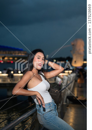 Asian tourist woman posing by the waterfront at Marina Bay Singapore during evening Asian tourist woman posing by the waterfront at Marina Bay Singapore during evening 137828669