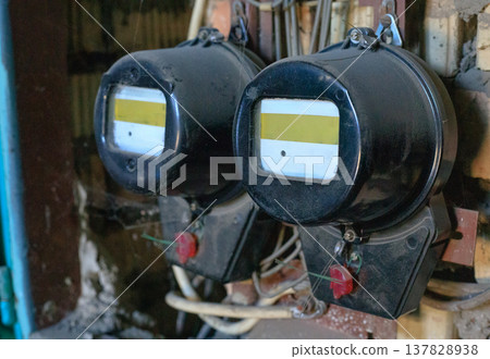 Two vintage, sealed electricity meters in an electrical panel in an old industrial building. The meters are connected to the power grid Two vintage, sealed electricity meters in an electrical panel in an old industrial building. The meters are connected to the power grid 137828938