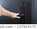 A woman opens a modern smart door lock with a digital keypad and biometric fingerprint access. 137829175