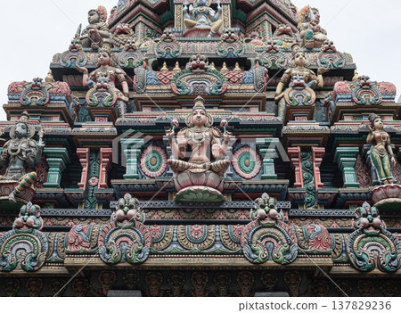 This image shows the vibrant, intricately carved gopuram of the Sri Maha Mariamman Temple. A central statue of Goddess Lakshmi is surrounded by tiered rows of deities and floral motifs, showcasing This image shows the vibrant, intricately carved gopuram of the Sri Maha Mariamman Temple. A central statue of Goddess Lakshmi is surrounded by tiered rows of deities and floral motifs, showcasing 137829236