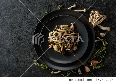 Fried shimeji mushrooms with thyme and garlic on a black plate. Fried shimeji mushrooms with thyme and garlic on a black plate. 137829242