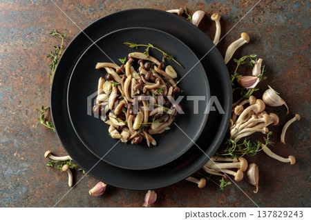 Fried shimeji mushrooms with thyme and garlic on a black plate. 137829243