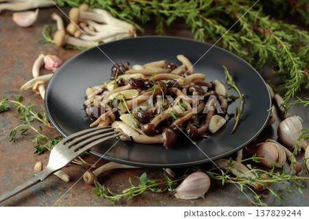 Fried shimeji mushrooms with thyme and garlic on a black plate. 137829244