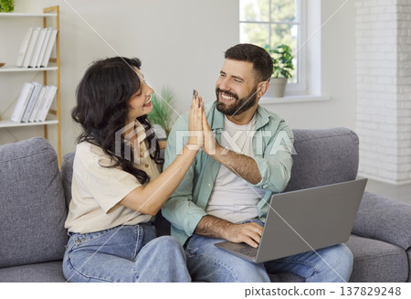 Couple celebrating successful payment with laptop at home, high five on sofa Couple celebrating successful payment with laptop at home, high five on sofa 137829248